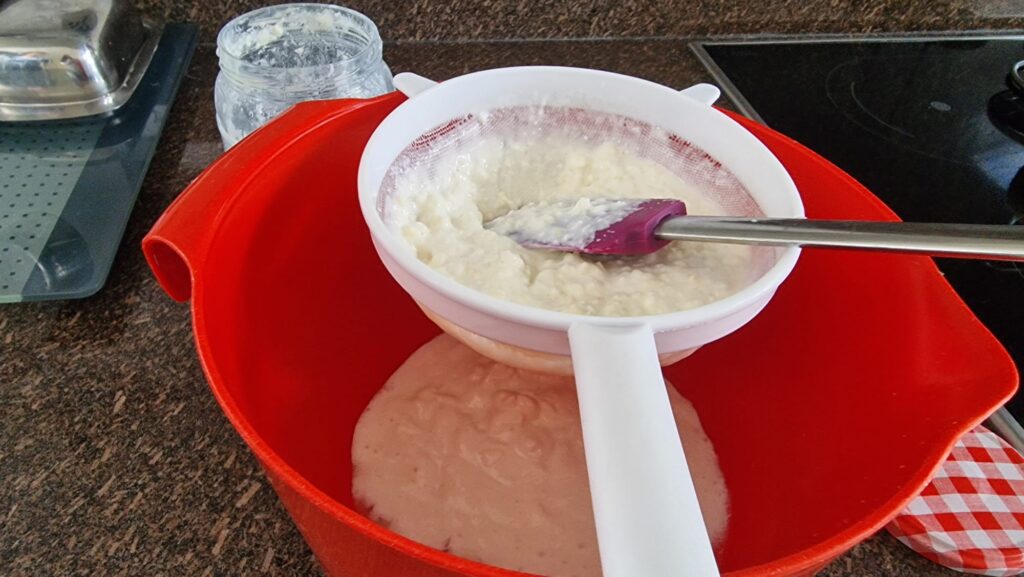 Straining homemade milk kefir through a plastic sieve into a bowl