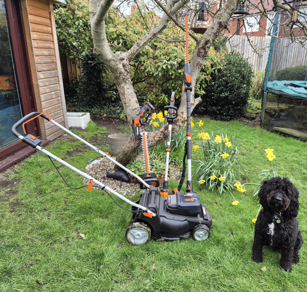 Worx PowerShare garden tools including cordless lawn mower, hedge trimmer and pole pruner in a UK garden