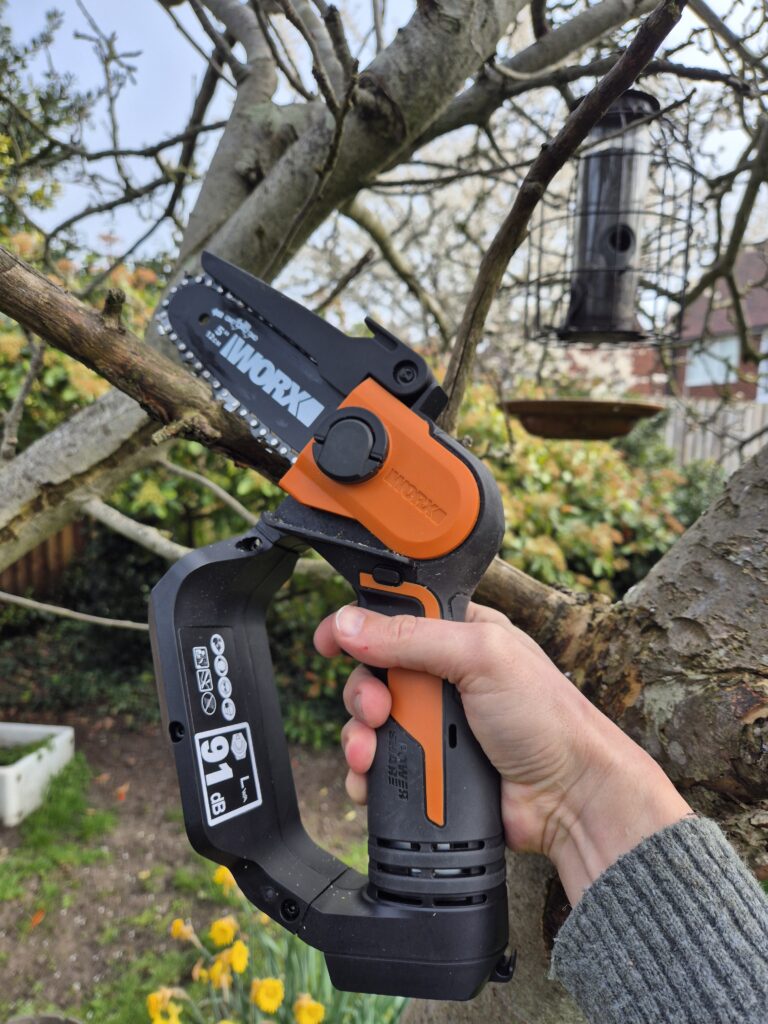Worx WG324E review showing the mini chainsaw cutting a branch in a UK garden