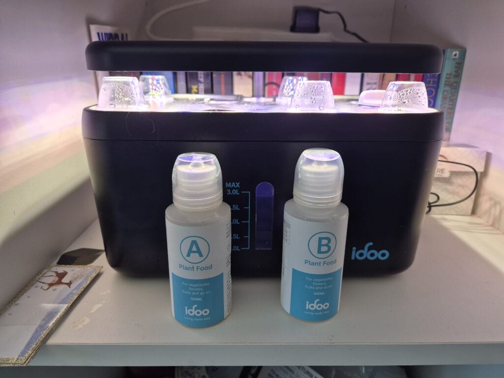 Hydroponic nutrients for beginners with iDOO A and B plant food bottles in front of an indoor hydroponic growing system